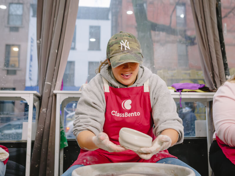 A person smiling and laughing at a pottery wheel throwing class